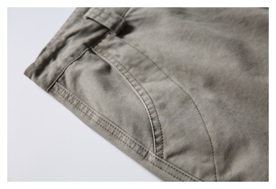 Close-up of gray-olive pants showing a curved front pocket opening and reinforced stitching.