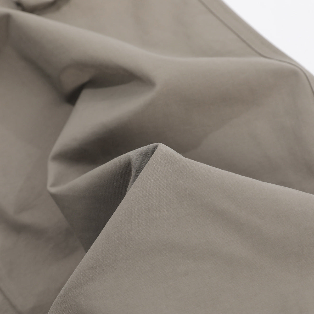 Close-up of the taupe-gray pants fabric, showing its smooth surface and drape.