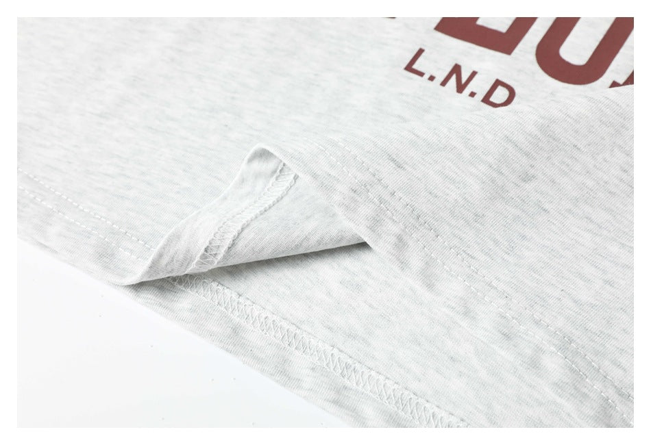 Close-up of the stitched hem on a light gray heather T-shirt, with part of its burgundy graphic visible.