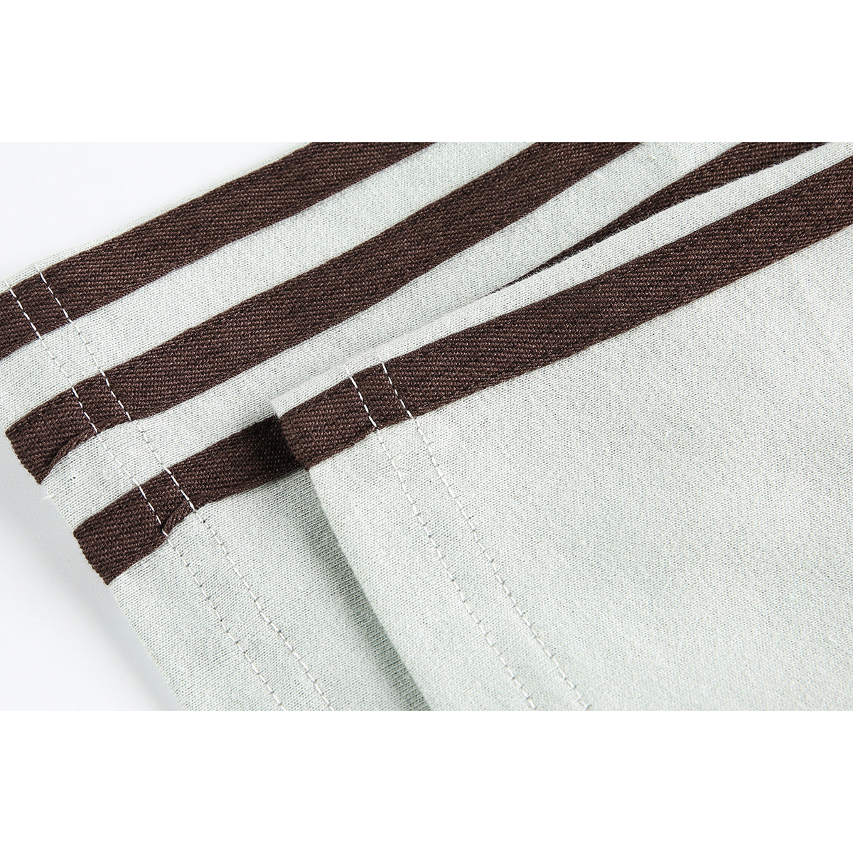 Close-up of pale fabric with dark brown stripes and parallel rows of stitching along a folded edge.