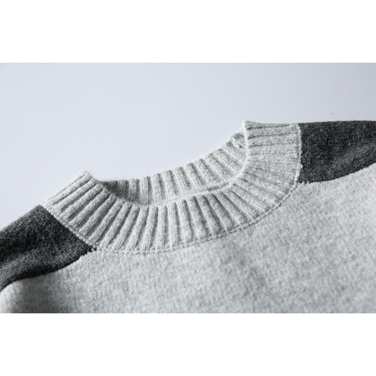 Close-up of a light gray sweater’s ribbed crew neck and dark charcoal shoulder panels.