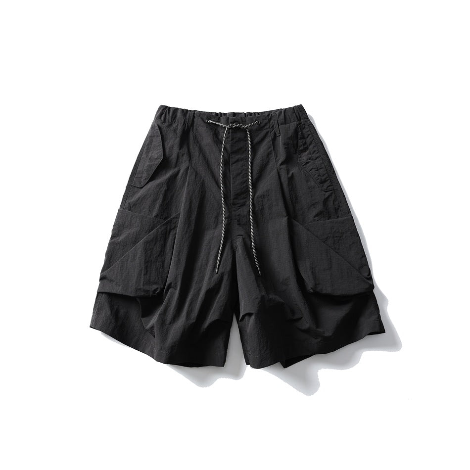 Black wide-leg knee-length shorts with large pleated hip pockets and a drawcord waist, flat lay