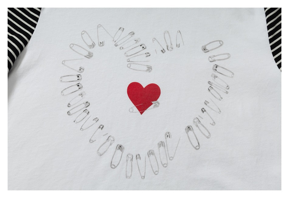 Close-up of a red heart surrounded by safety-pin illustrations printed on a white T-shirt.