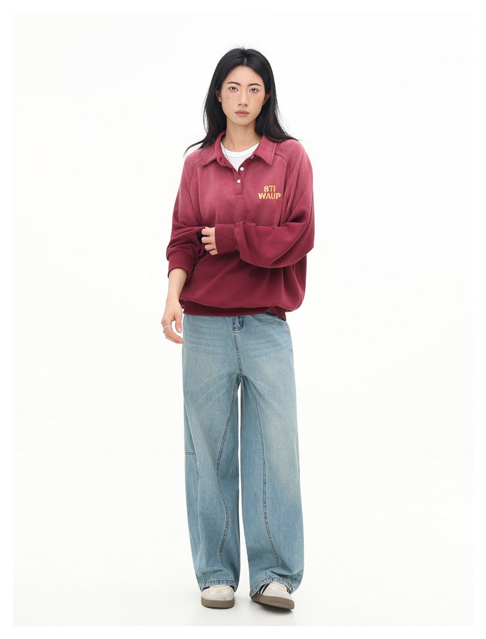 Full-length front view of a model in a rose-red collared pullover with yellow chest lettering and wide-leg light blue jeans.