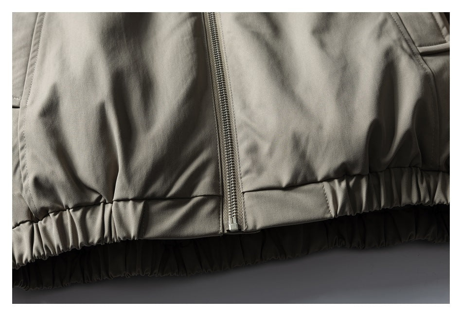 Close-up of a gray-beige jacket's front zipper and gathered elastic hem.