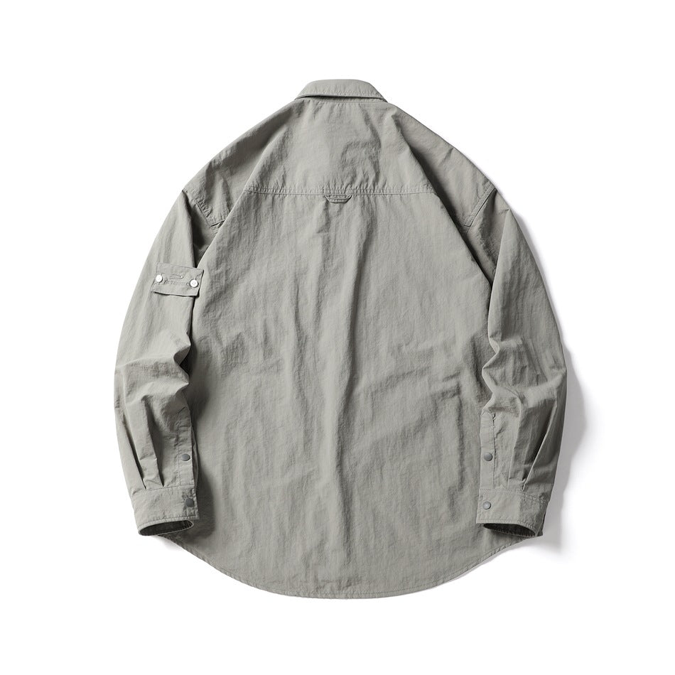 Back view of a light gray-green long-sleeve shirt with a pointed collar, curved hem, and snap-button cuffs.