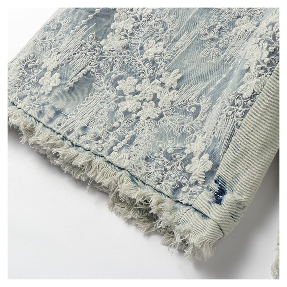 White floral embroidery decorates a faded blue denim panel above its frayed edge.