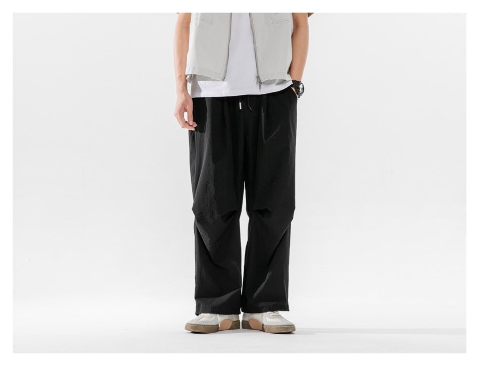Person wearing black wide-leg drawstring pants with a white tee and light gray vest, front view cropped at the torso