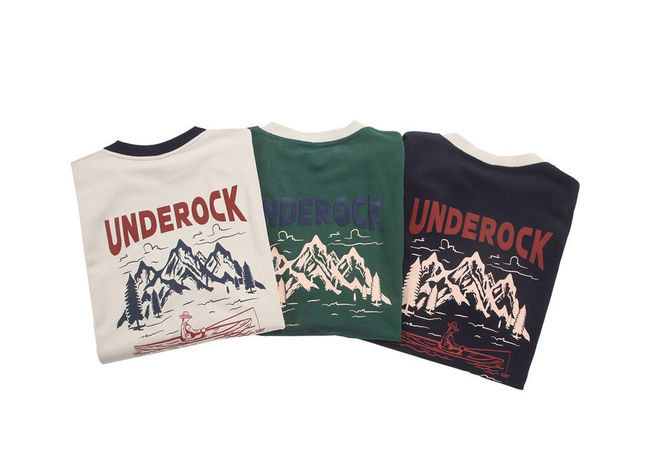 Three folded shirts in beige, forest green, and navy display large mountain, lake, and canoe graphics.