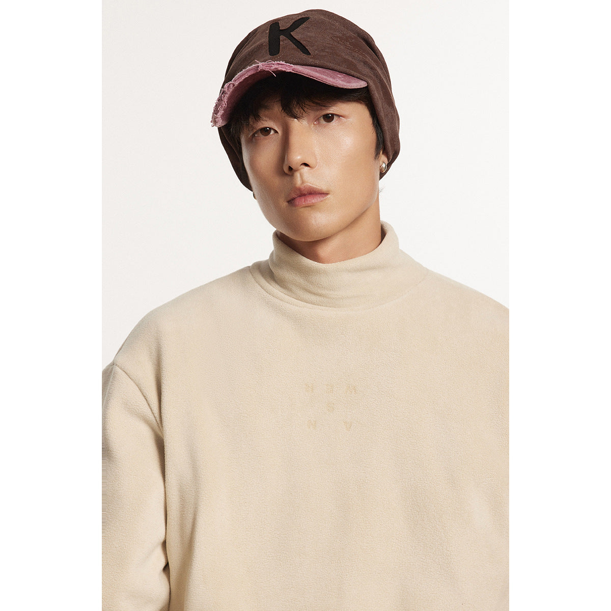 Close-up of a model in a cream high-neck pullover and brown cap with a pink brim.