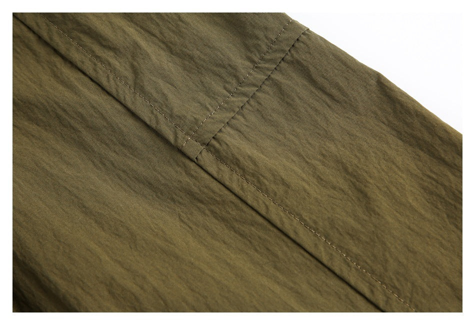 Close-up of olive-brown garment fabric showing a diagonal stitched seam and narrow fabric tab.