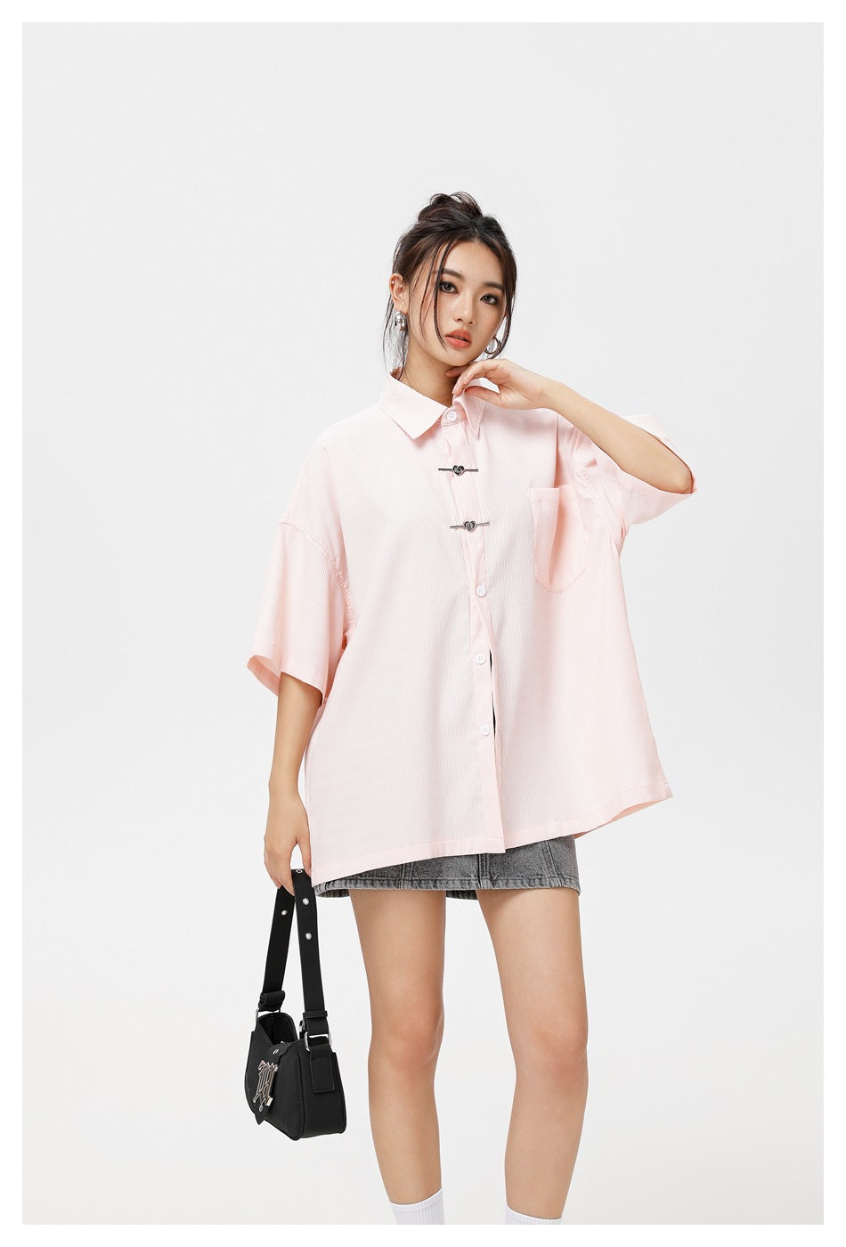 Model wearing a pale pink oversized short-sleeve button-up shirt with decorative clasps and a chest pocket.
