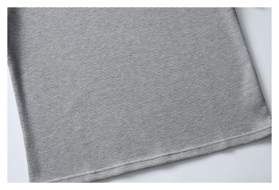 Close-up of the stitched bottom hem on a gray textured garment.
