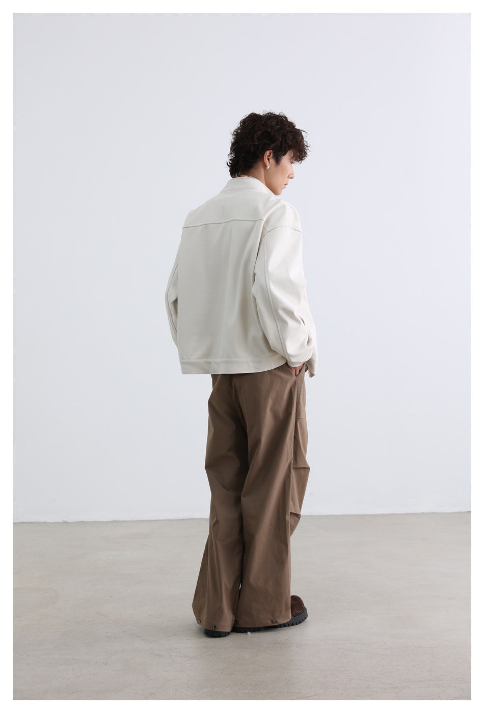 Rear three-quarter view of a model wearing an off-white jacket and taupe trousers.