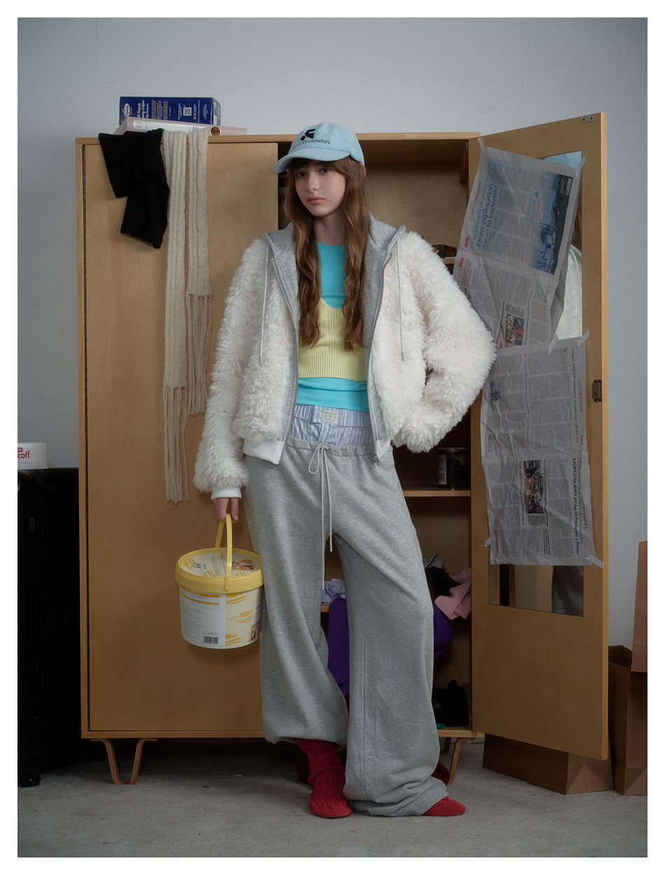 Model wearing the white fleece-like hooded zip jacket open over a layered top with gray sweatpants and a light blue cap