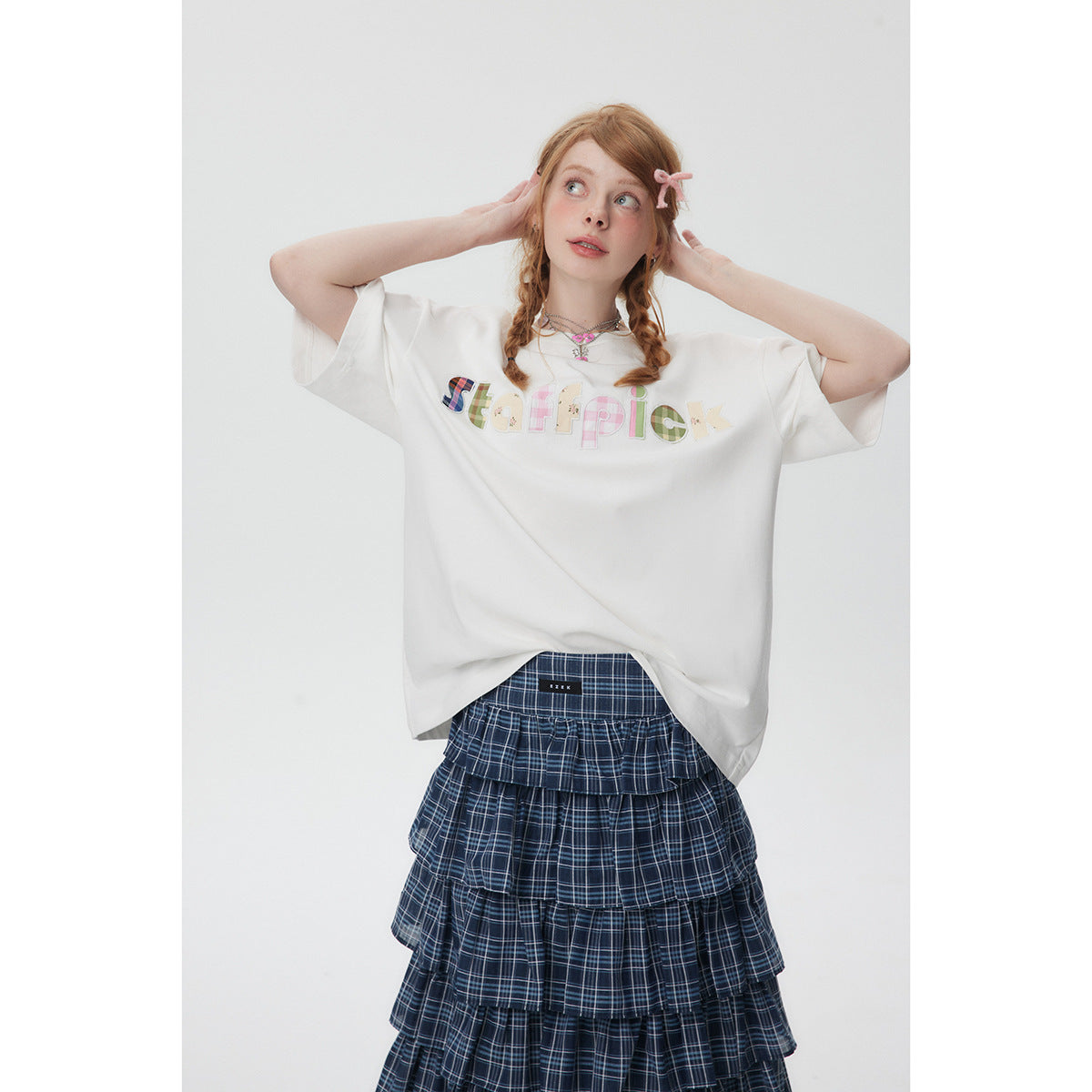 Model wearing an oversized white T-shirt with colorful patchwork lettering and a navy plaid tiered skirt.