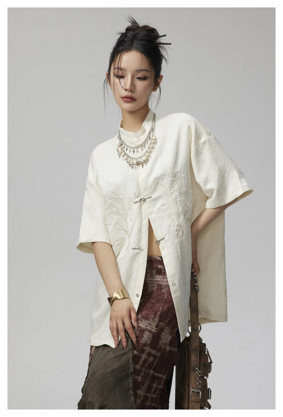 Model wearing an ivory embroidered tunic with a stand collar and frog closures, paired with a patterned skirt.