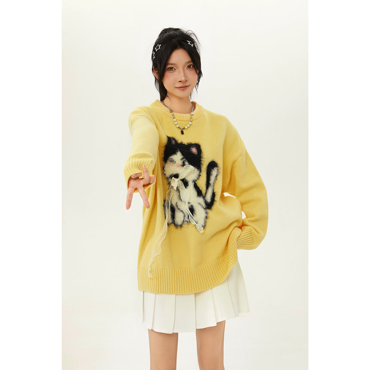 Model wearing a yellow oversized sweater with a fluffy cat applique and a white pleated skirt.