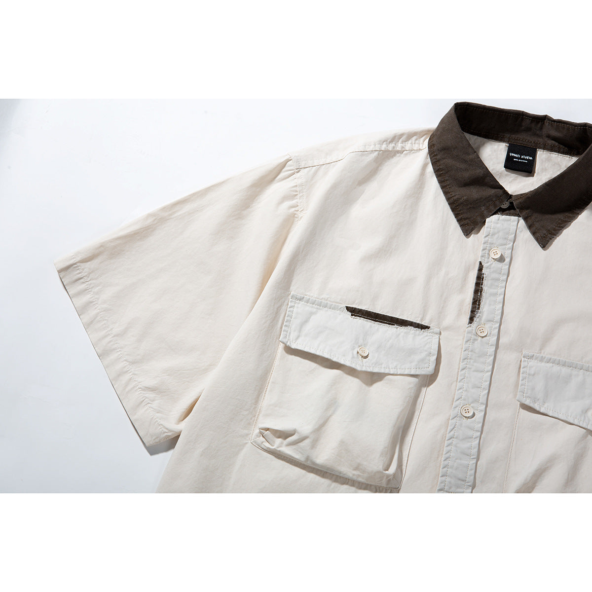 Angled close-up of an off-white shirt showing its wide short sleeve, dark brown collar and flap chest pockets.