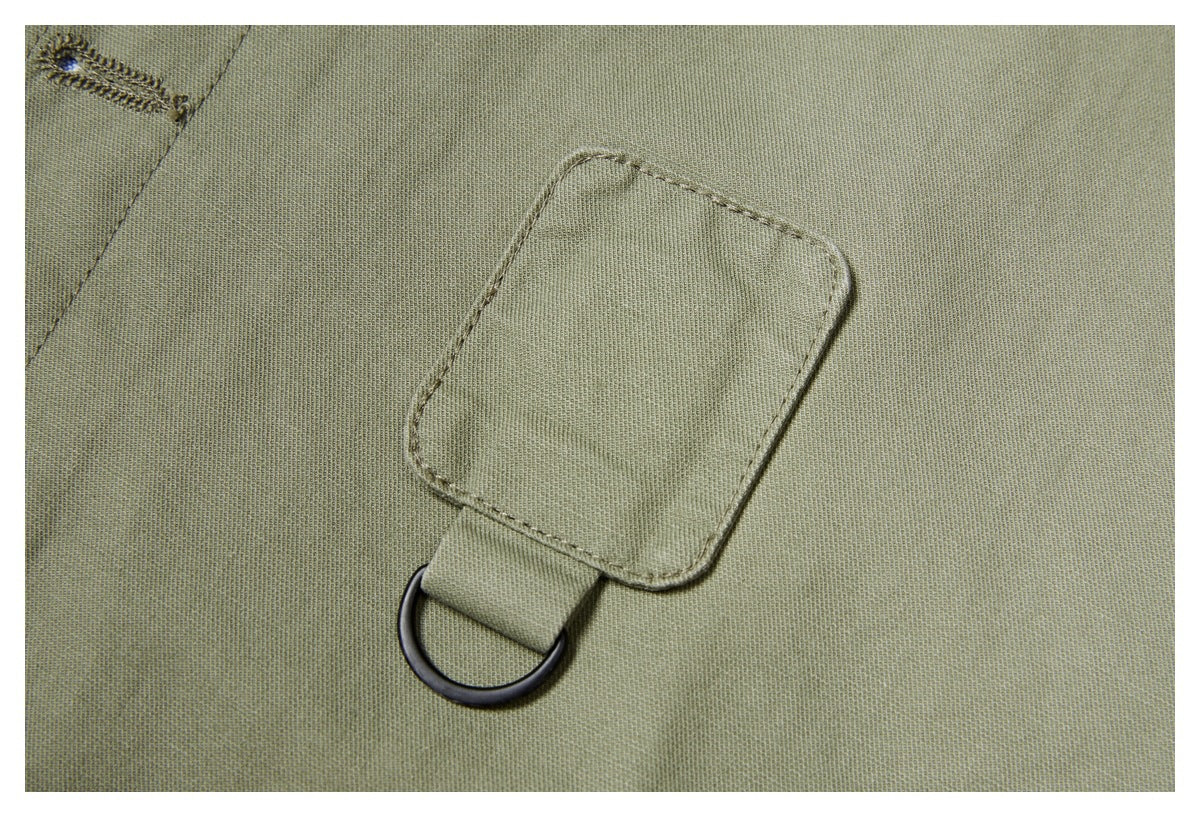 Close-up of an olive-green shirt showing a stitched fabric tab and dark metal D-ring.
