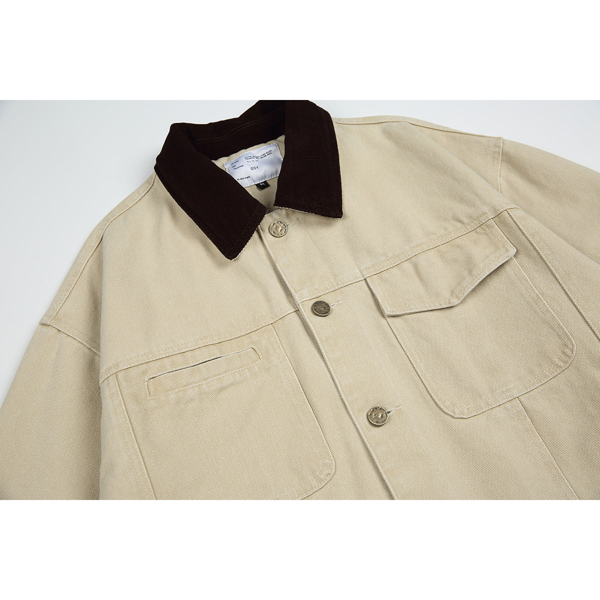 Close-up of a beige jacket front with a dark brown collar, metal buttons and large flap pockets.