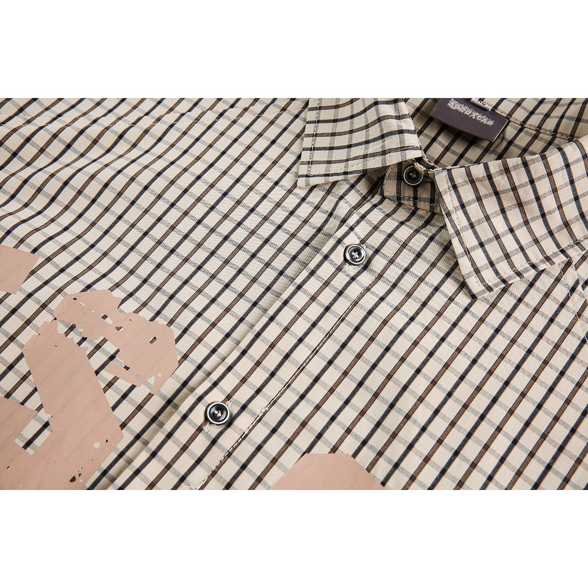 Close-up of a beige checked shirt showing its collar, buttons, and distressed chest graphic.