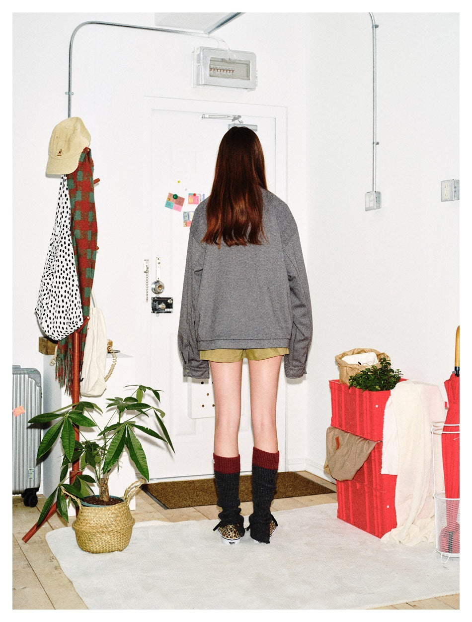 Rear view of a model wearing an oversized gray jacket with olive shorts and tall dark socks.