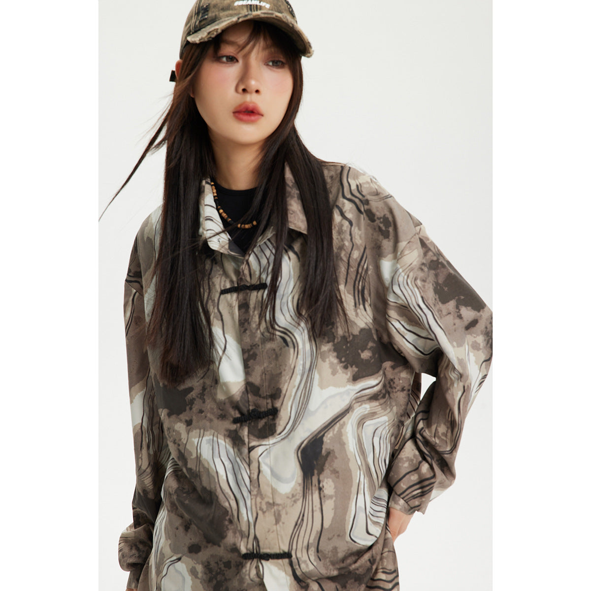 Model wearing a taupe and cream abstract-print shirt with black frog closures and a camouflage cap.