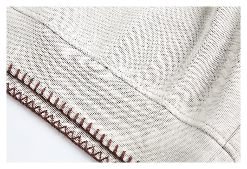 Close-up of a cream garment hem with brown blanket stitching and zigzag edging.