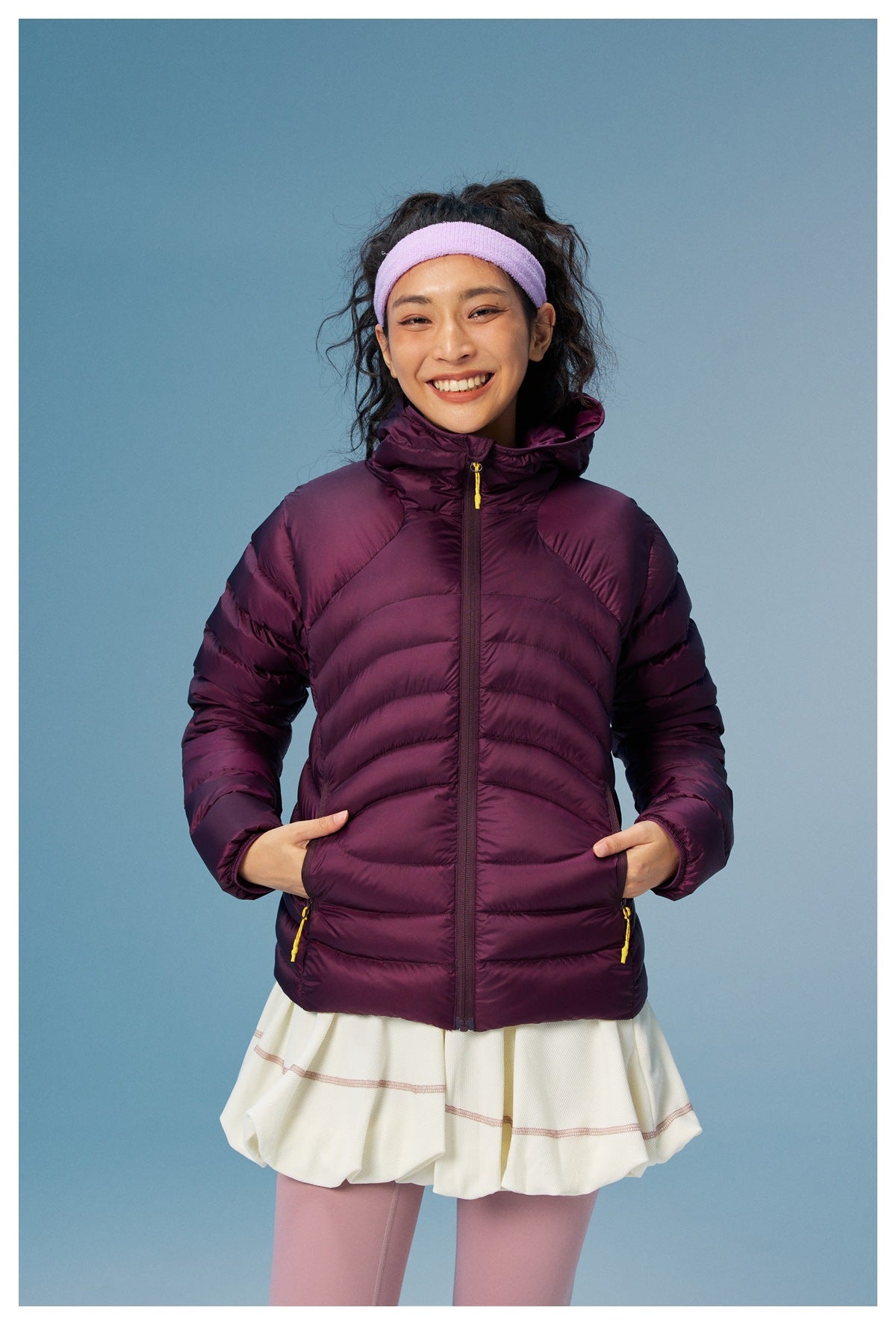 Front view of a model wearing a plum hooded quilted jacket with curved seams and yellow pocket zipper pulls.