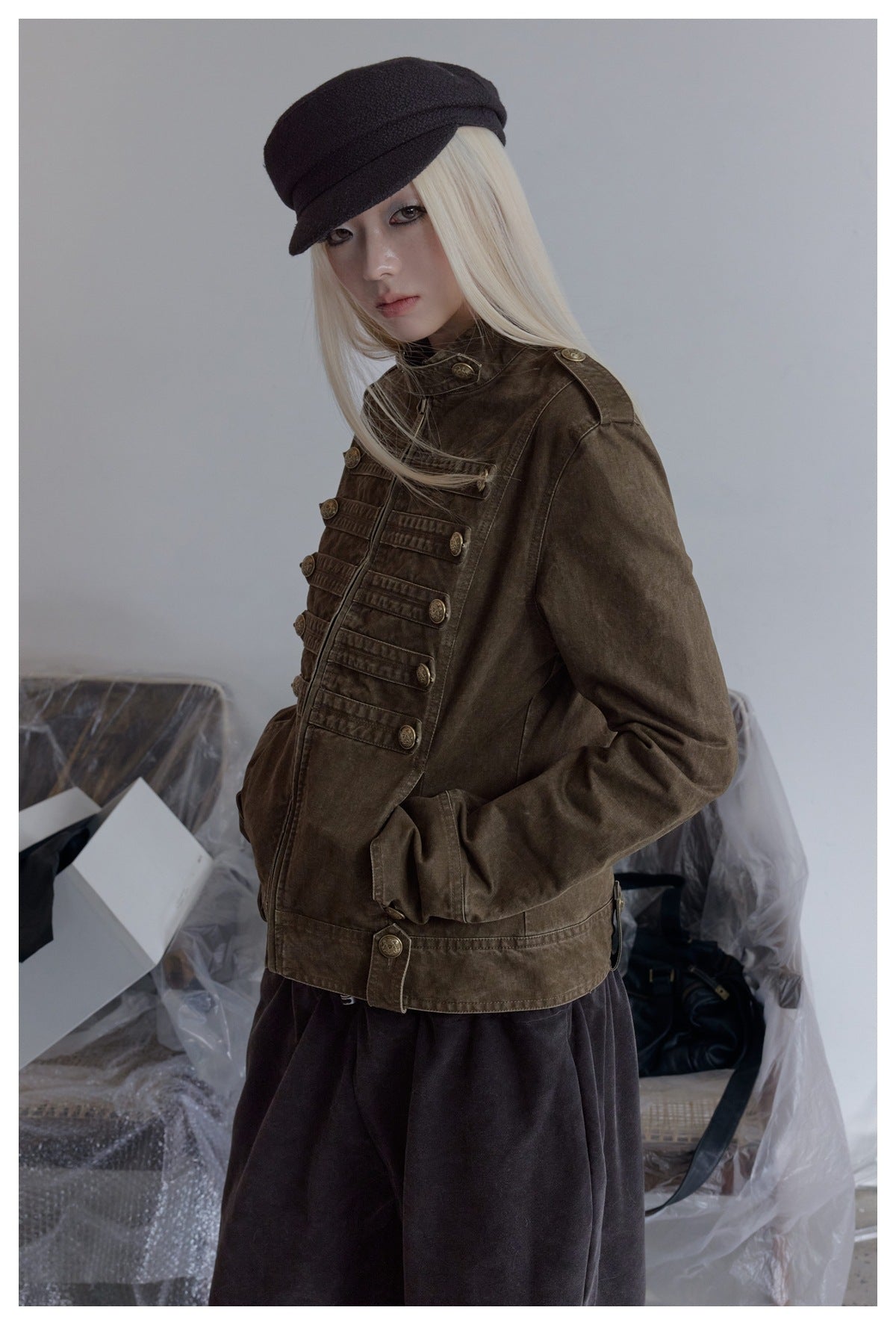 Three-quarter view of a model wearing a dark olive-brown jacket with a high collar and ornate button detailing.