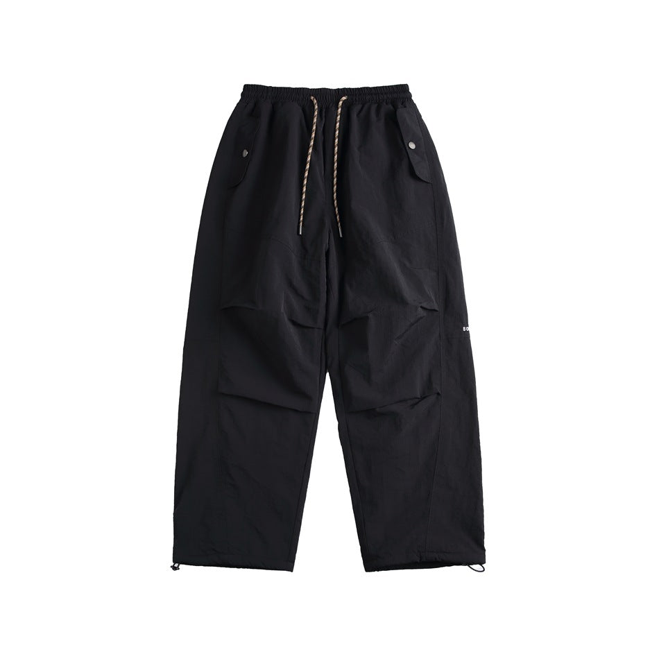 Black wide-leg nylon-look pants with drawstring waist, snap flap pockets and toggle hems, front flat lay