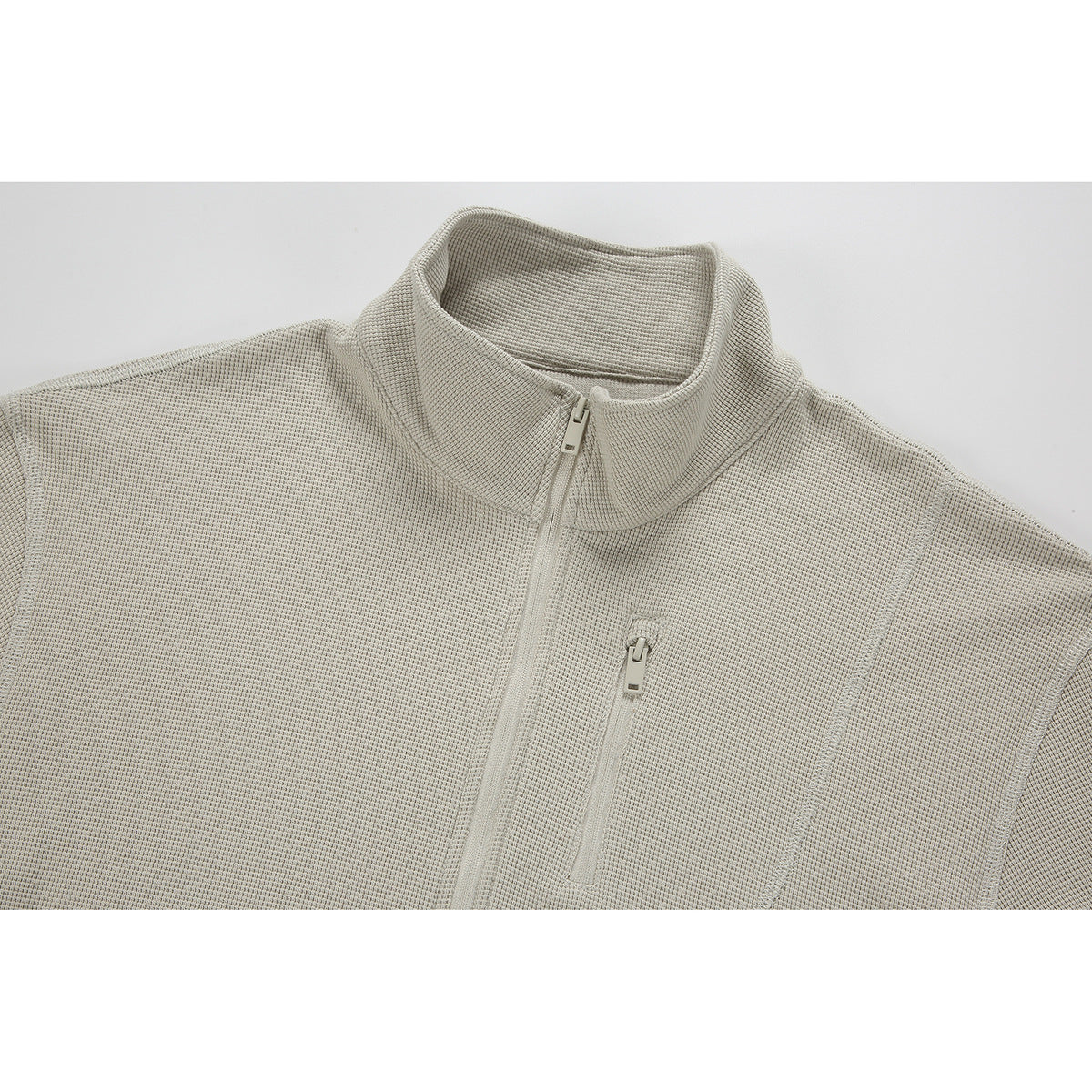 Close-up of a light beige textured pullover with a stand collar, front zipper, and zippered chest pocket.