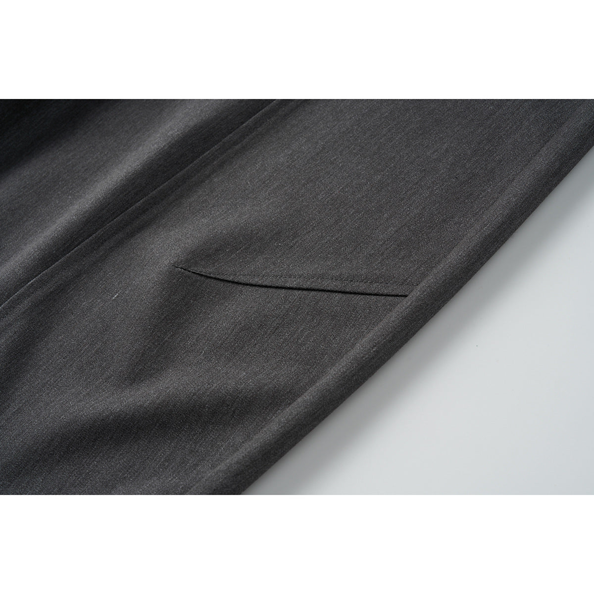 Close-up of charcoal gray trouser fabric and a narrow welt pocket.