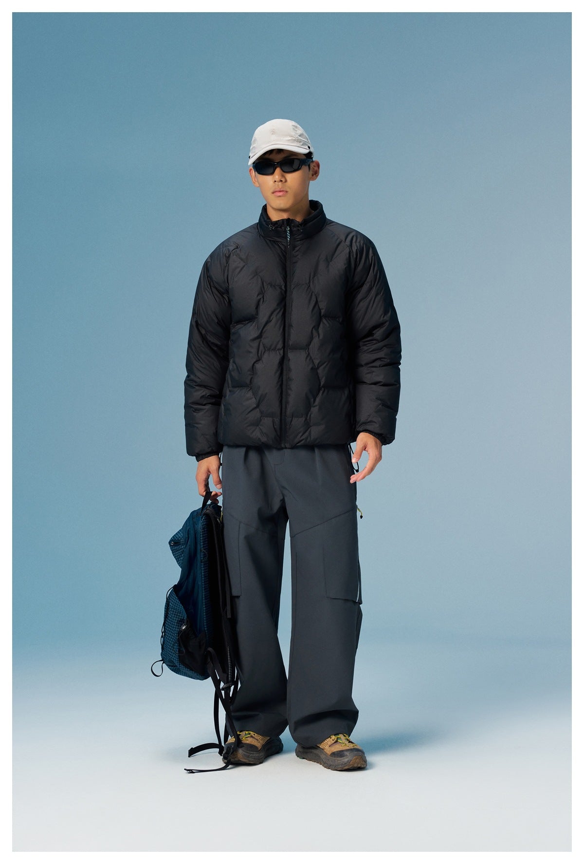 Full-length model wearing a black quilted zip jacket and wide dark cargo pants, holding a backpack.