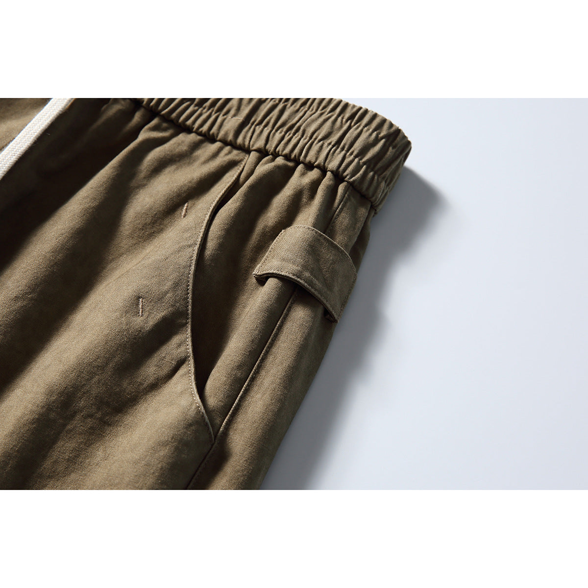 Close-up of olive-brown cargo pants showing a side pocket and flap cargo pocket beneath the elastic waist.