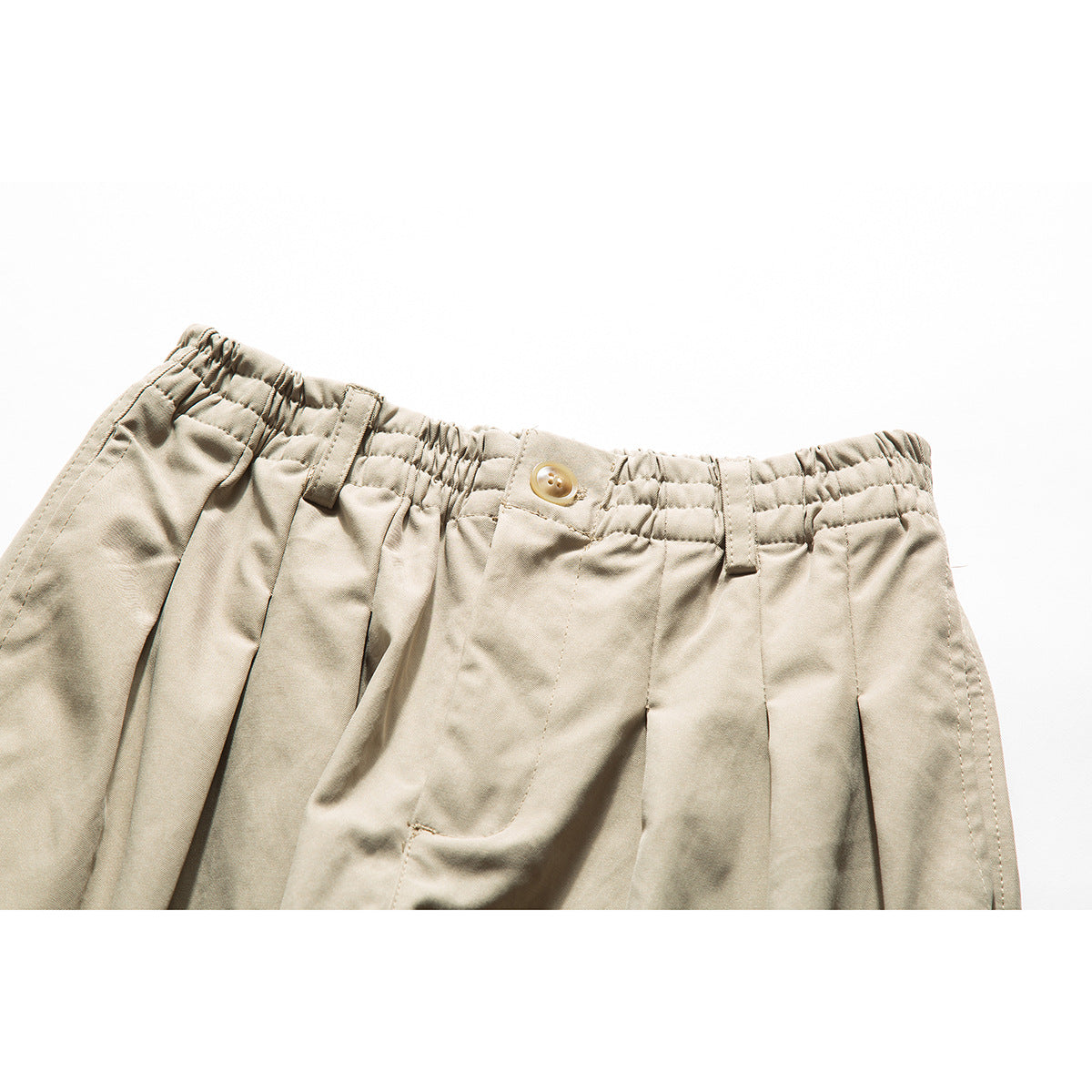 Close-up of beige trousers showing the gathered waistband, button, belt loops, and front pleats.