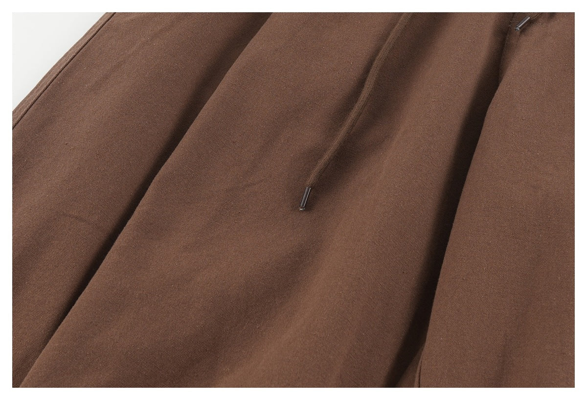 Close-up of brown trouser fabric and a dangling drawstring with a metal tip.