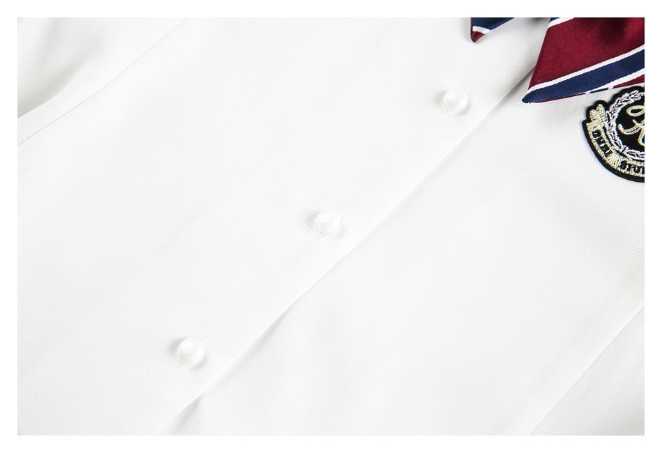 Close-up of a white shirt placket with white buttons and a burgundy-and-navy striped collar beside an embroidered crest.