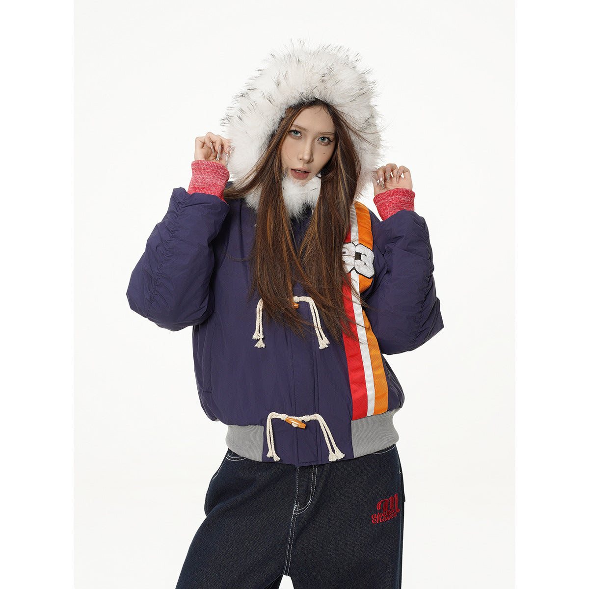 Model wearing a navy hooded jacket with white faux-fur trim, red cuffs, orange-red stripes and rope toggles.