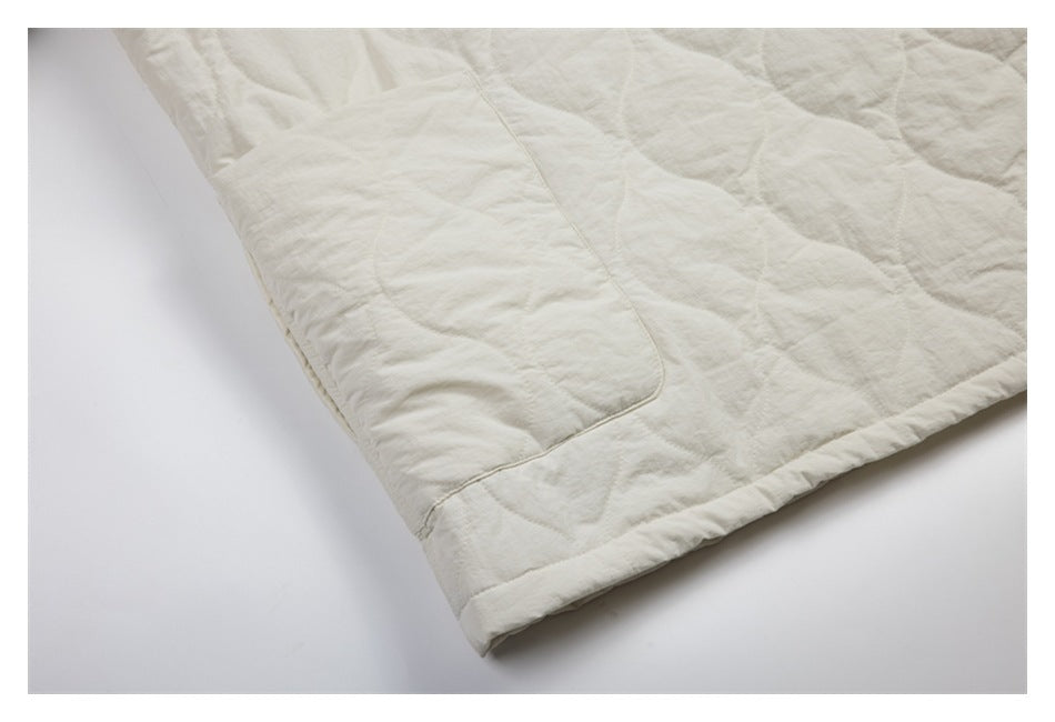 Close-up of an ivory quilted jacket hem and large rectangular patch pocket.