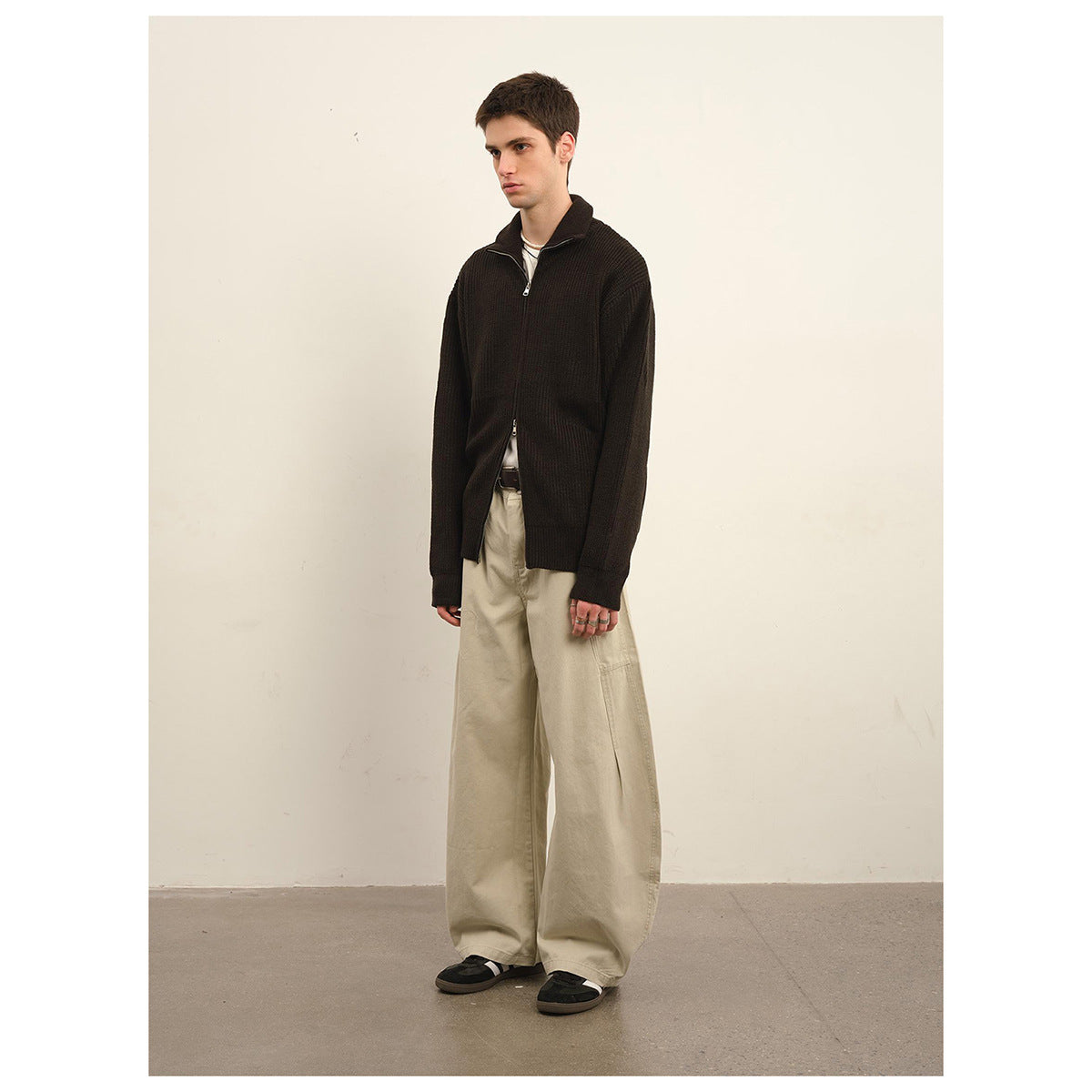 Model wearing a dark brown ribbed zip-front sweater with a high collar and loose beige trousers.