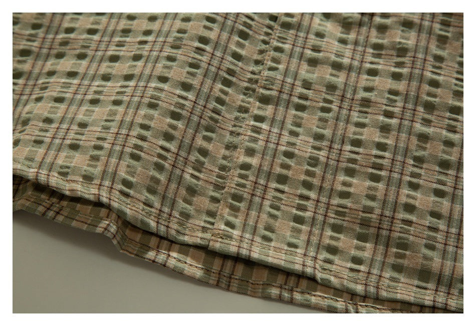 Close-up of the olive and tan plaid shirt's stitched lower hem and patterned fabric.