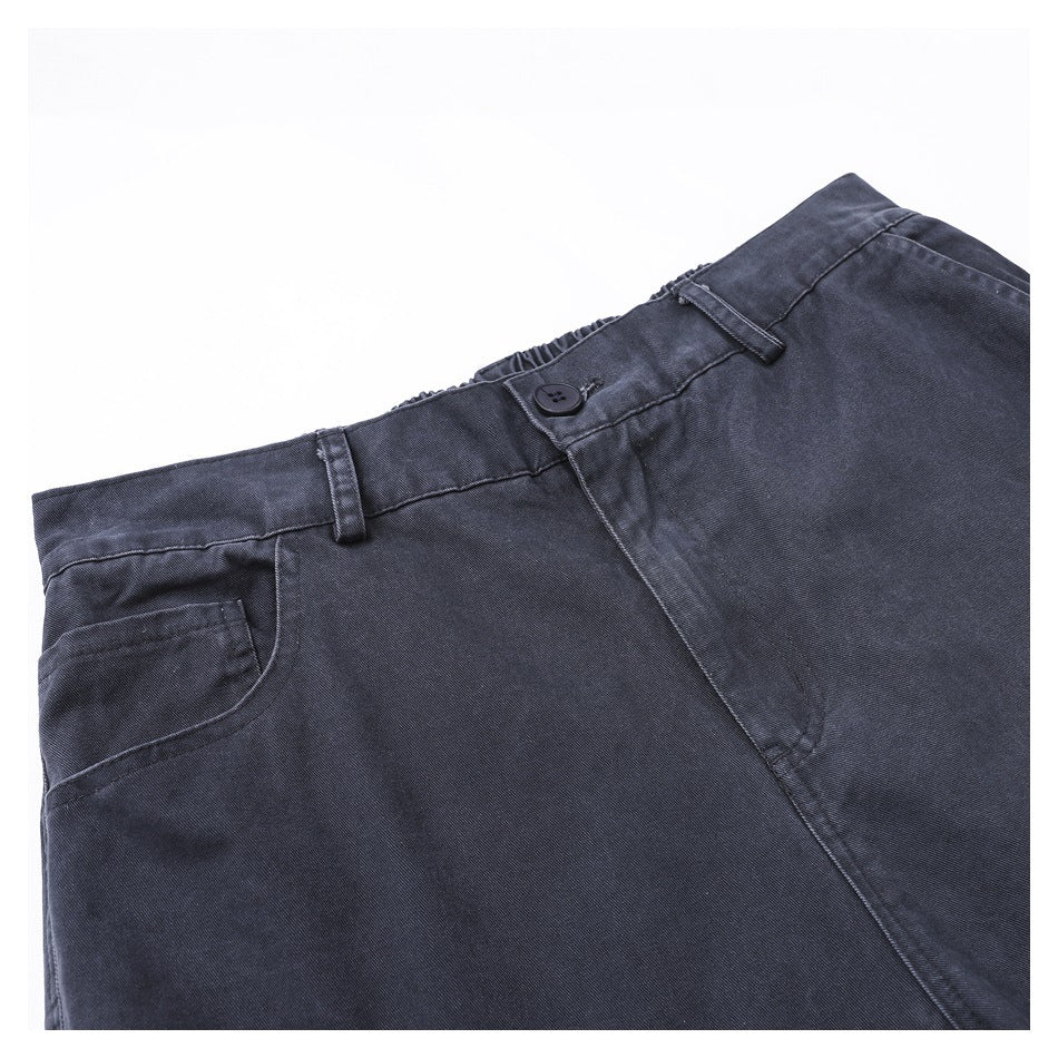 Close-up of charcoal trousers showing the front waistband, button, belt loops and curved pocket.