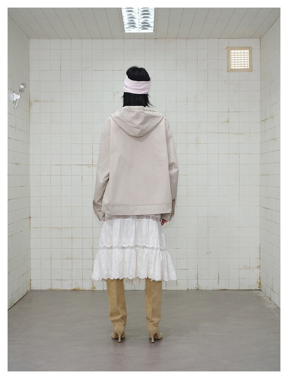 Back view of a model wearing a plain beige hooded jacket over a white tiered lace skirt.
