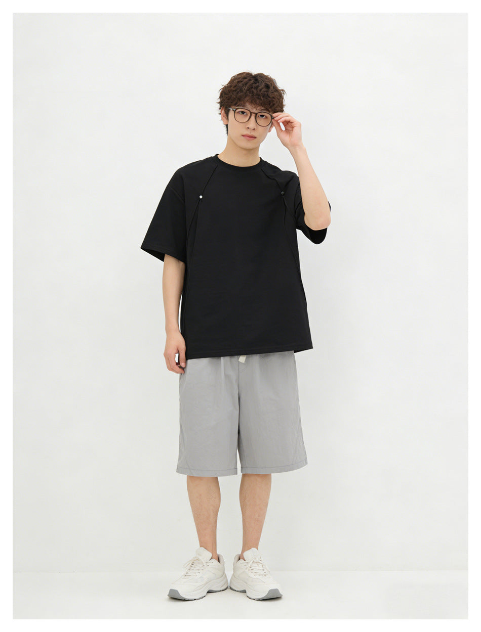 Front view of a model wearing a black short-sleeve crew-neck shirt with shoulder seams and small fasteners.