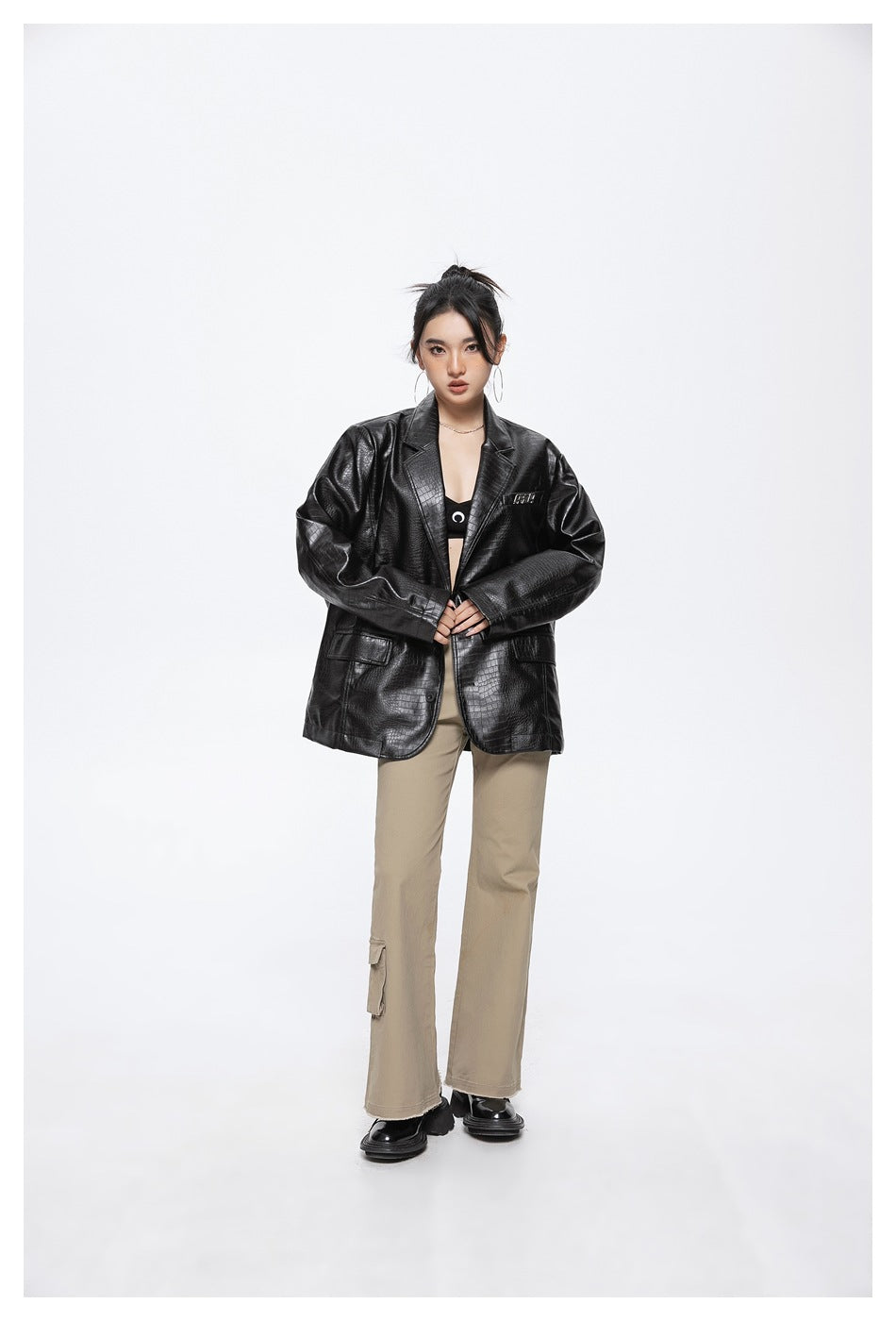Front view of a model wearing an oversized black crocodile-textured blazer and beige cargo trousers.