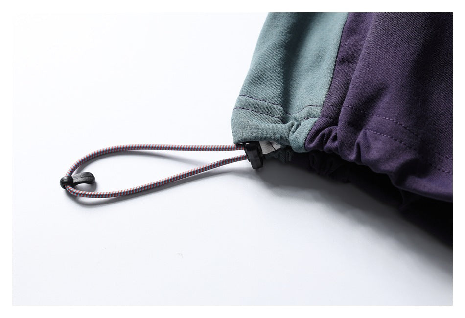 Close-up of a garment hem with a multicolored drawcord and black toggle beside teal and purple fabric.