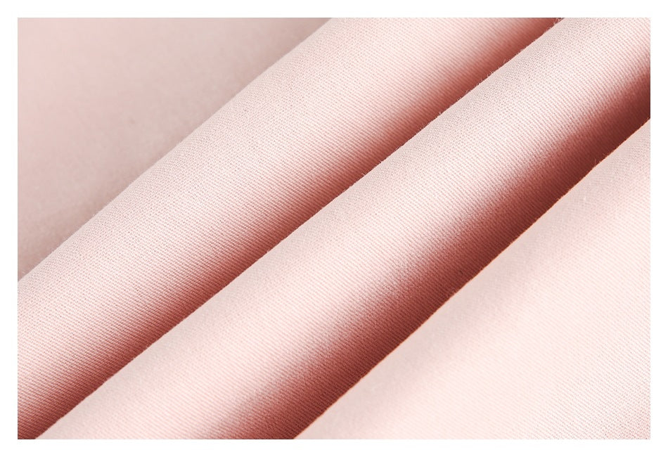 Close-up of pale pink fabric folded into soft diagonal ridges, showing its fine texture.