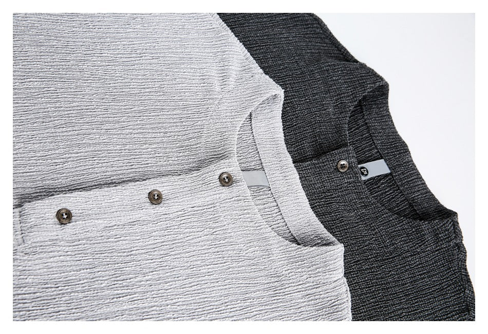 Close-up of light gray and charcoal tops showing textured fabric, round necklines, and button plackets.